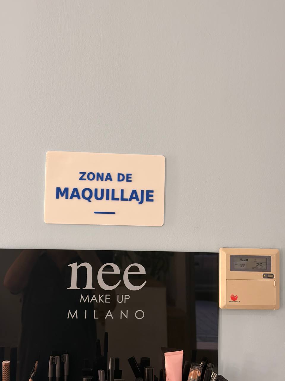 Rótulo blanco con el texto ZONA DE MAQUILLAJE en azul sobre la pared